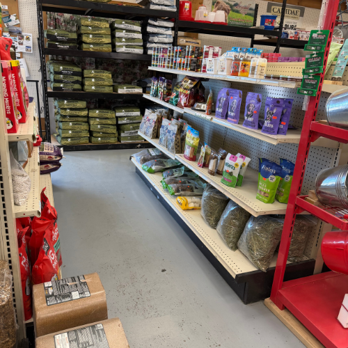 Pet store aisle stocked with bags of pet food, treats, litter, and supplies on shelves; bright, orderly displays create a practical shopping scene.