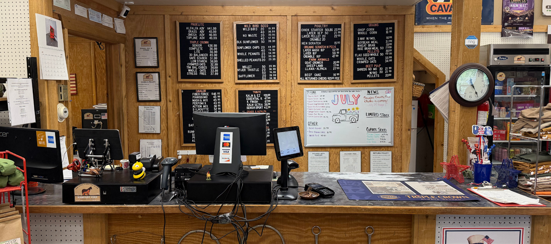 Cozy wood-paneled café counter with chalkboard menus, cash registers, coffee equipment, a wall clock, and colorful signs behind the service area.